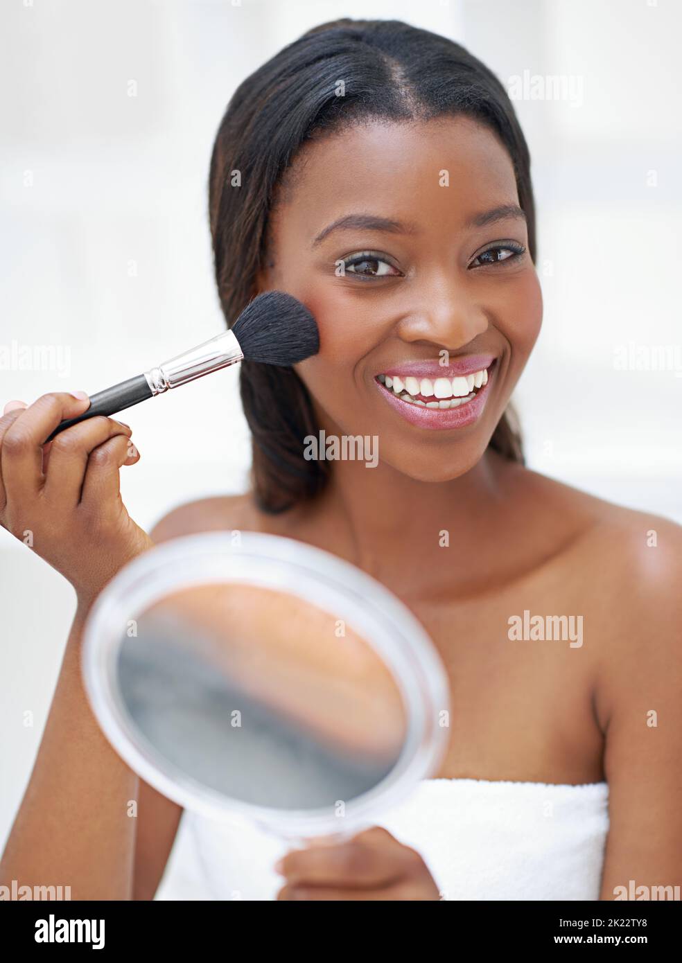 This is the best blush ever. a beautiful young woman applying blush with a makeup brush Stock