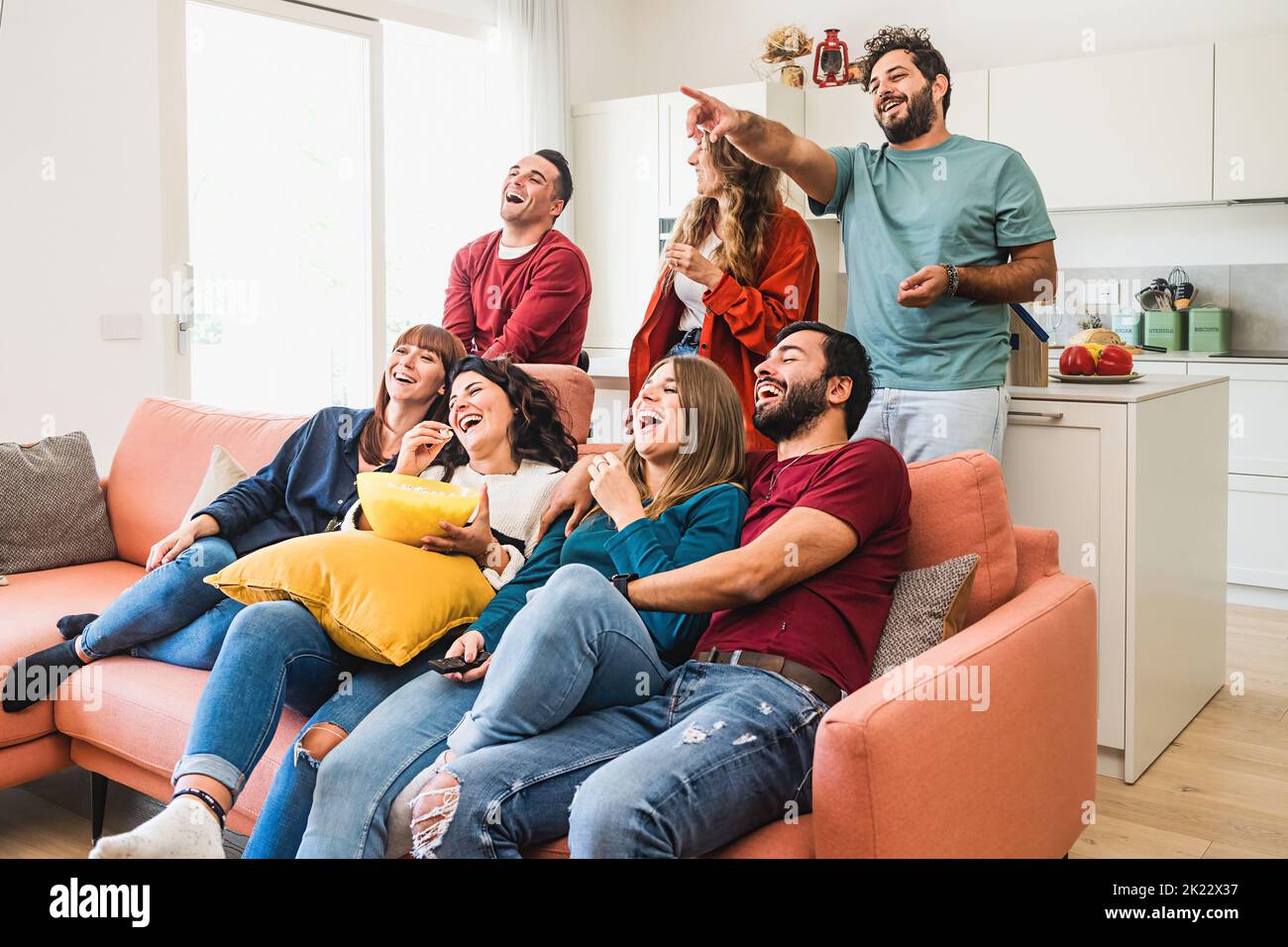A group of young adults people enjoy watching funny content such as comedy movie on TV while eating popcorn, the bearded guy points on the television Stock Photo