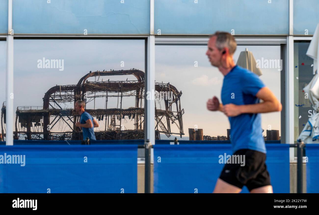 Brighton UK 22nd September 2022 - Runners reflected in windows by Brighton West Pier in early morning sunshine as more unsettled weather is forecast for the next few days .   . : Credit Simon Dack / Alamy Live News Stock Photo