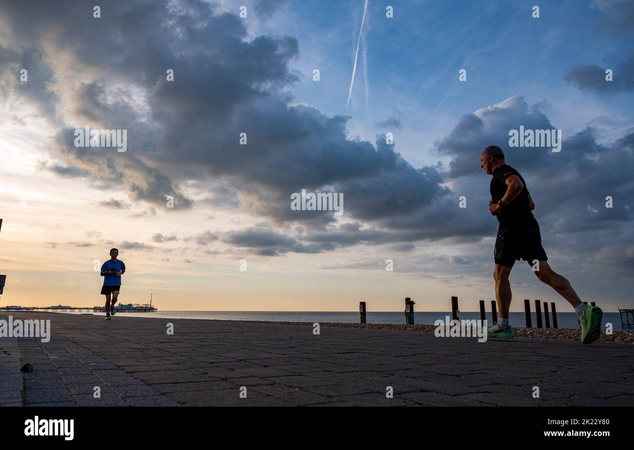Brighton UK 22nd September 2022 - Runners pass under  dark clouds and early morning sunshine over Brighton seafront as more unsettled weather is forecast for the next few days .   . : Credit Simon Dack / Alamy Live News Stock Photo