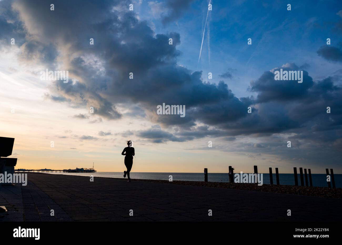 Brighton UK 22nd September 2022 - A runner passes under  dark clouds and early morning sunshine over Brighton seafront as more unsettled weather is forecast for the next few days .   . : Credit Simon Dack / Alamy Live News Stock Photo