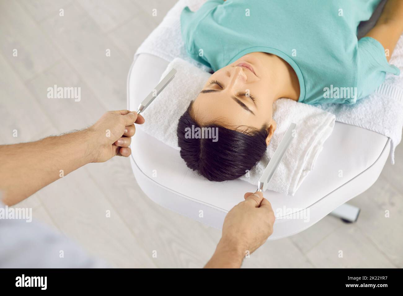 Holistic healer using two tuning forks during sound therapy session with young woman Stock Photo