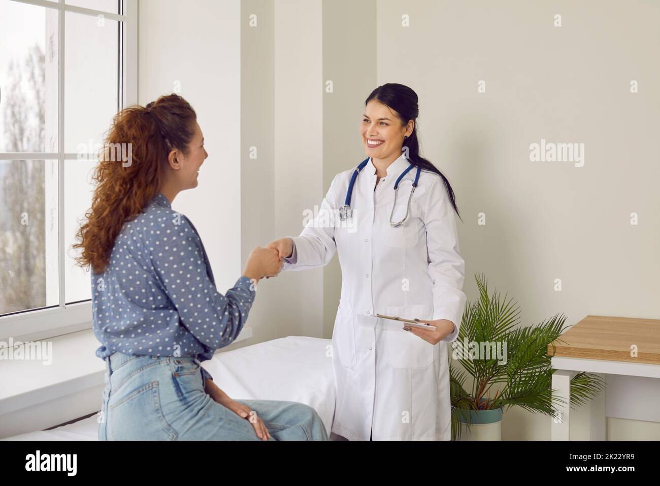 Friendly female doctor shakes hands with her patient welcoming her to appointment in her office. Stock Photo