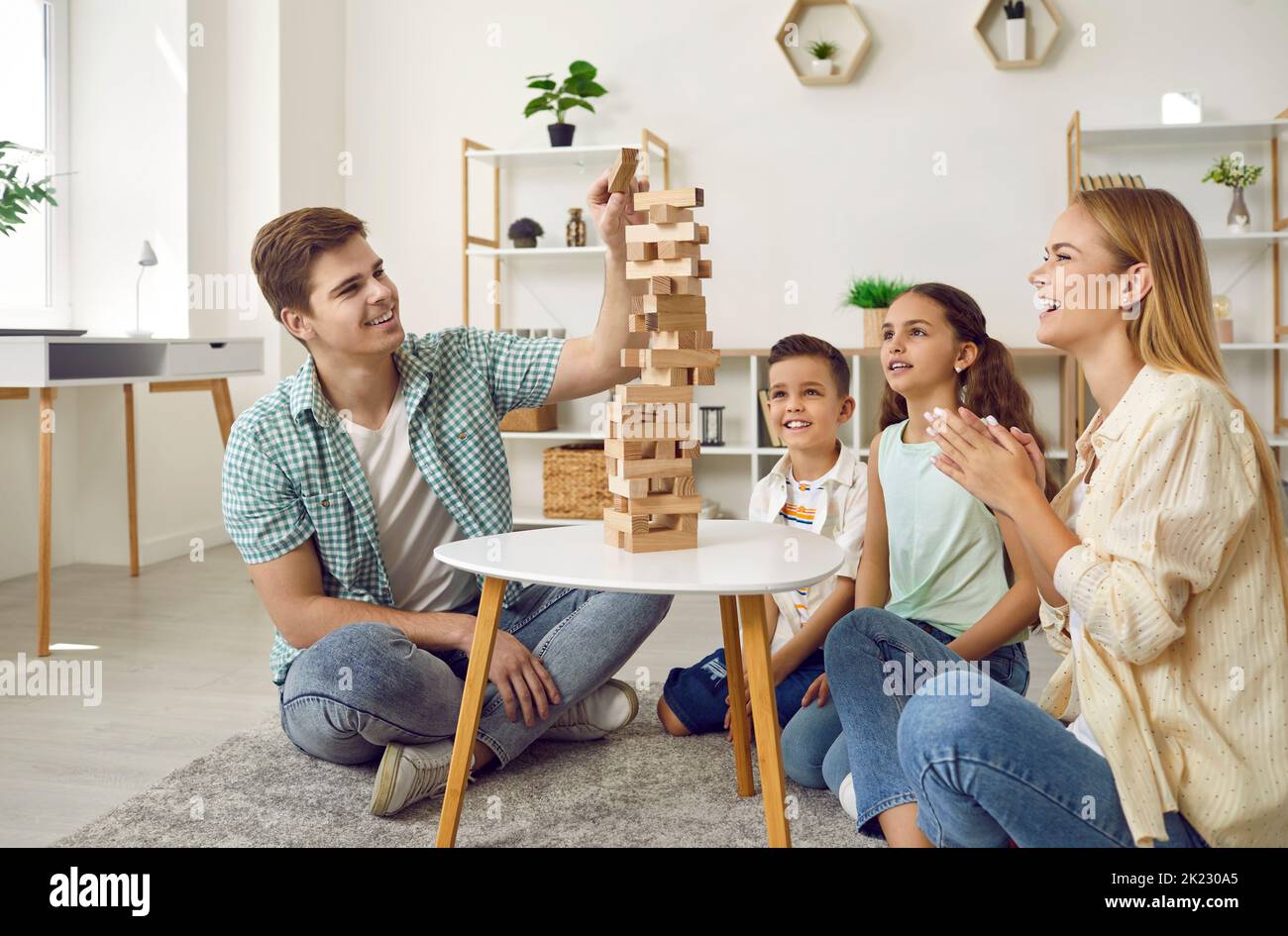 Young parents and their two young children are having fun playing Jenga together. Stock Photo