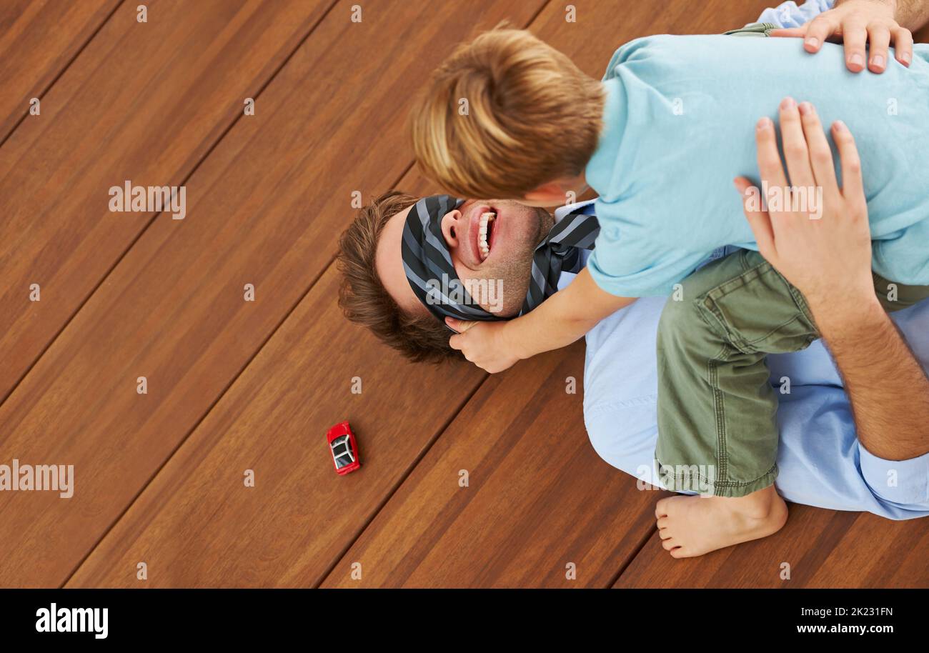 You cant see me. A cute boy sitting on his young father and covering his eyes with his tie. Stock Photo