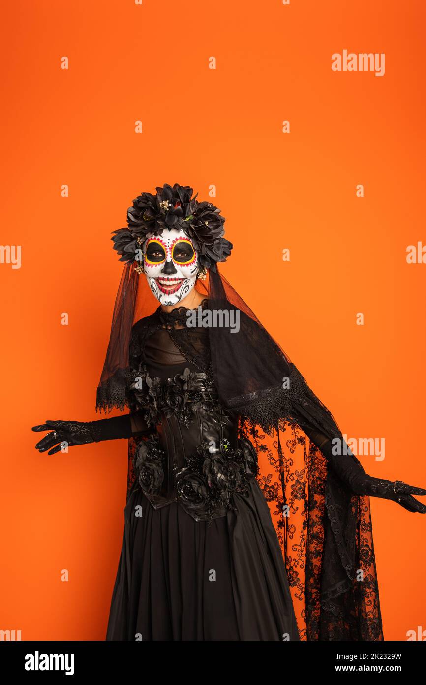 smiling woman in black witch dress and spooky halloween makeup isolated on  orange,stock image Stock Photo
