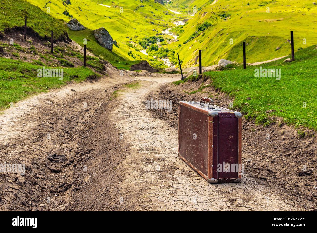 Old shabby leather suitcase on a dirt road in the mountains Stock Photo