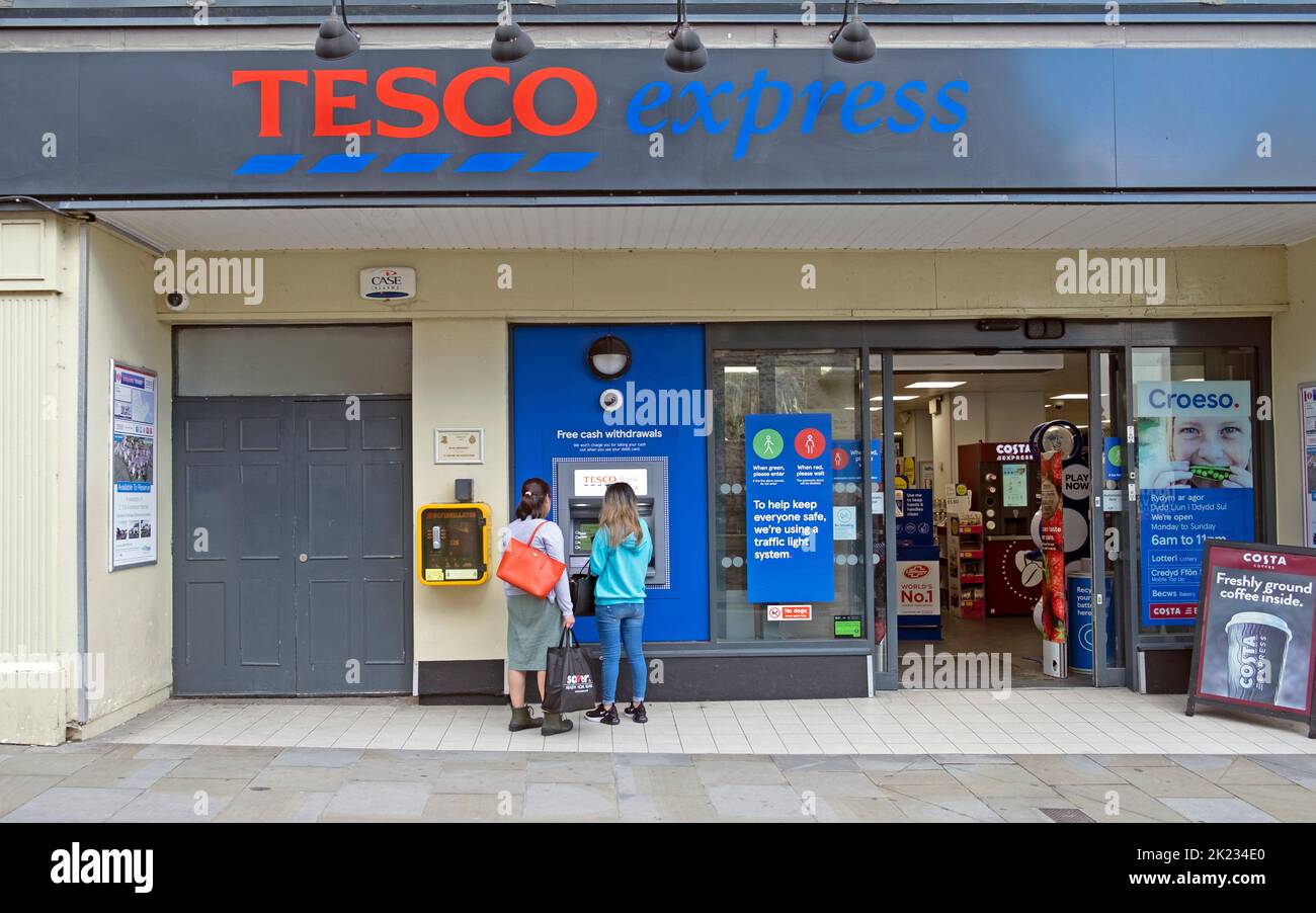 Exterior view of Tesco Extra storefront customers people using ATM machine cash point outside grocery store in Tenby Pembrokeshire South Wales UK Stock Photo