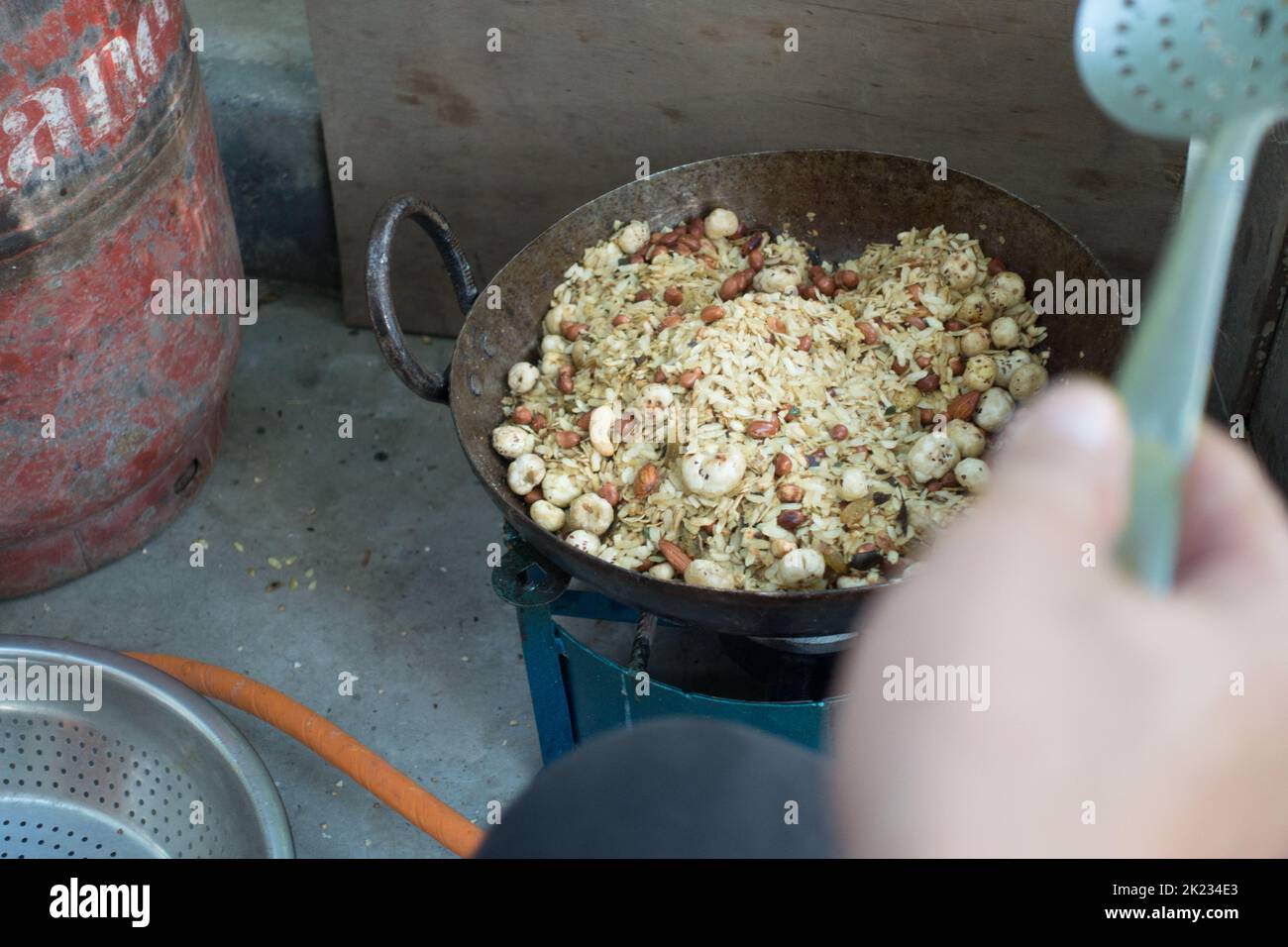 Preparing Homemade granola with oats, buckwheat, nuts and seeds in a big cast iron cauldron or kadai on a traditional stove. Uttarakhand India Stock Photo