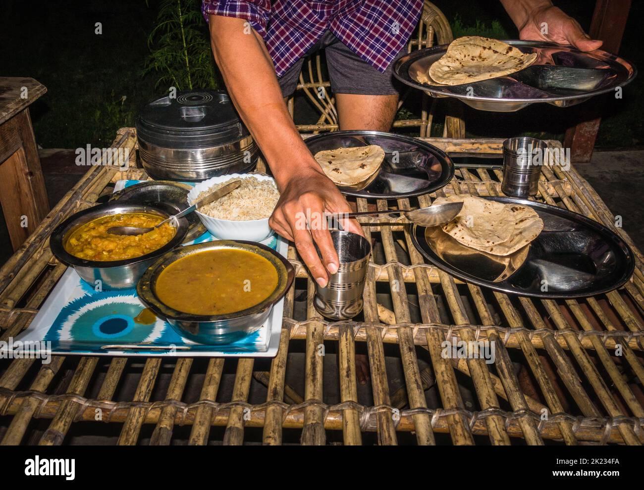 A man serving Indian meal of Rice, dal and chapati on a traditional bamboo table top. Stock Photo