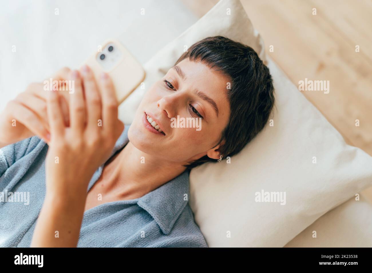 Young happy smiling modern woman lying on pillows on the bed texting in
