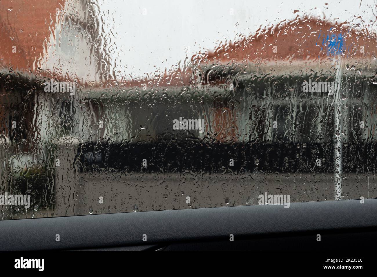 Car window with rain drops on windshield. Blurred orange roof buildings outside on a rainy day. Dunedin, New Zealand. Stock Photo