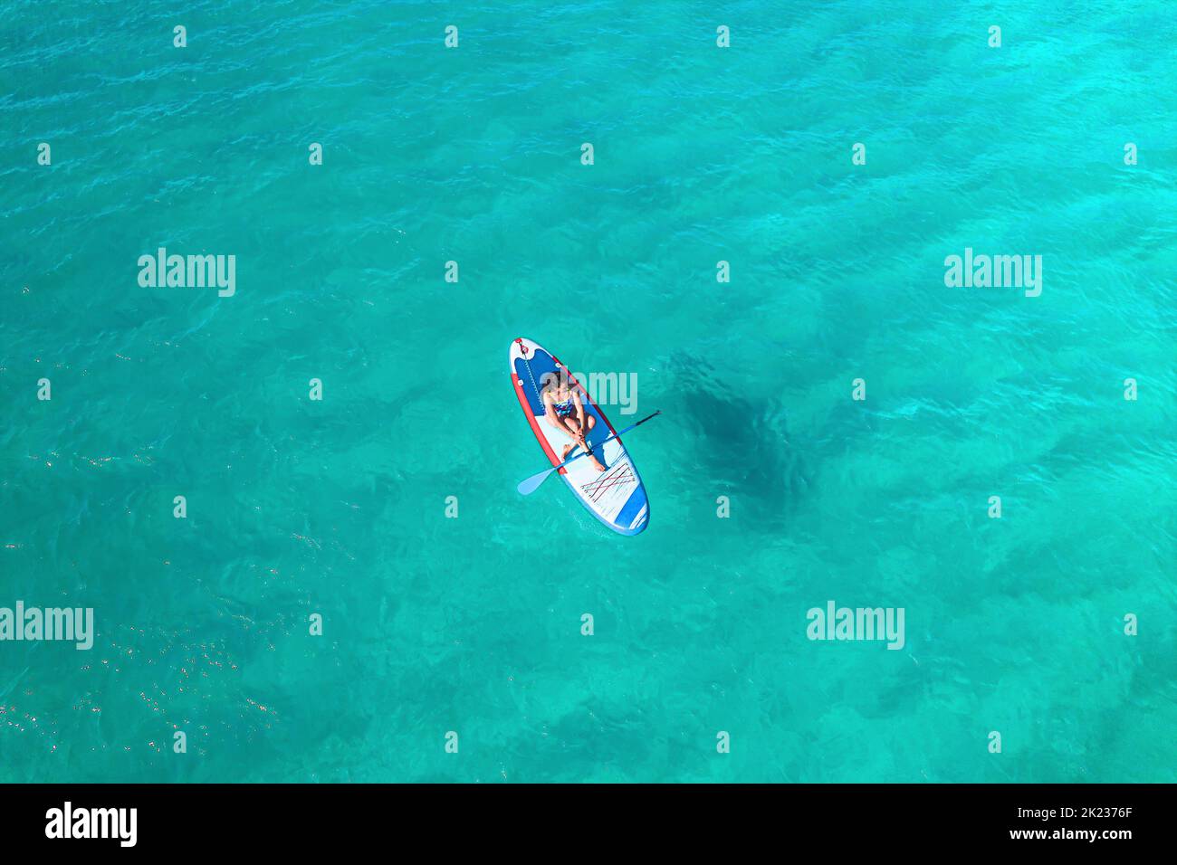 The drone photo of the crystal clear water of the Adriatic Sea in Croatia and a girl sitting on the sup board Stock Photo