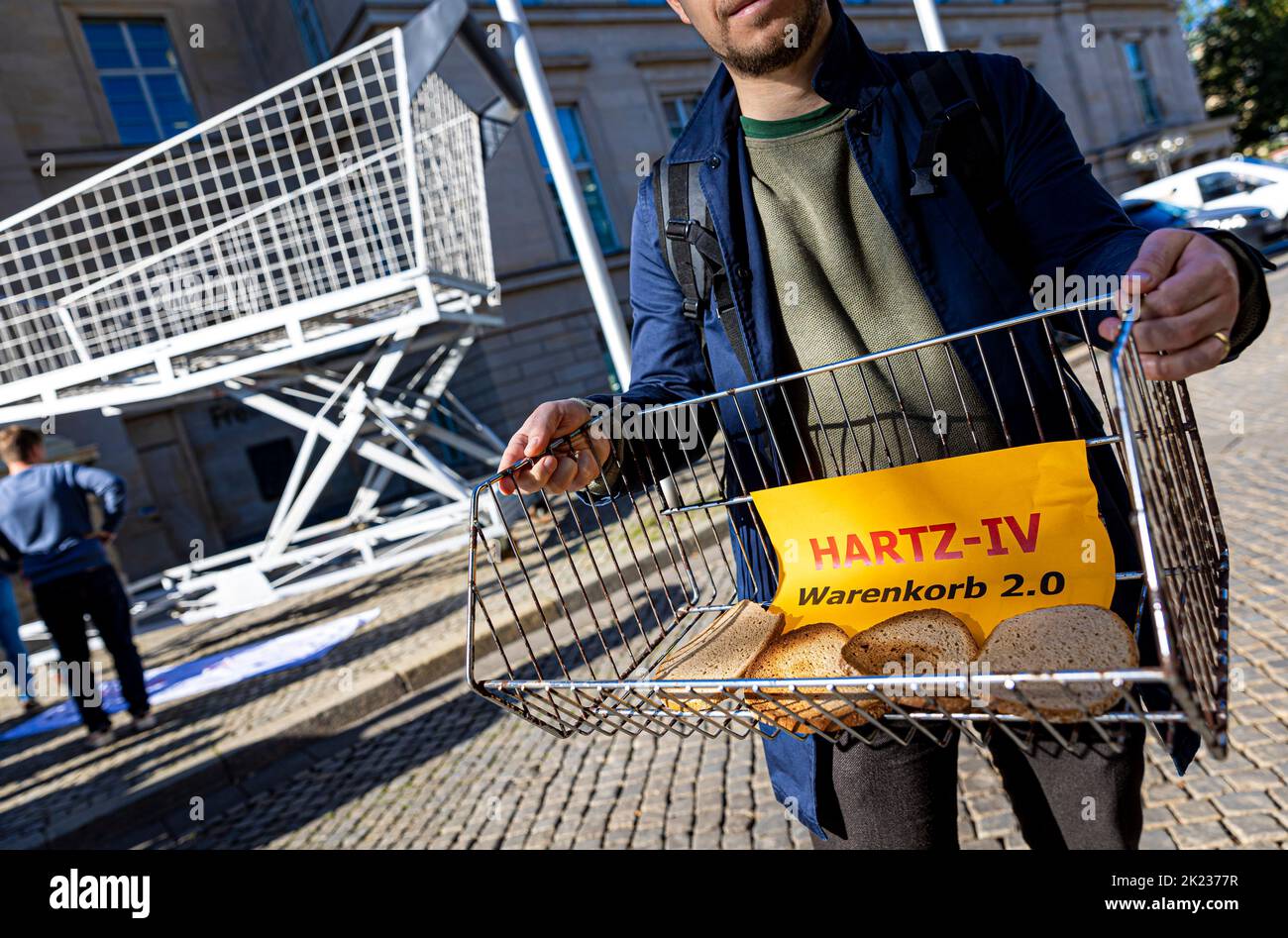Hanover, Germany. 22nd Sep, 2022. The words 'Hartz-IV Warenkorb 2.0' (Hartz IV shopping cart 2.0) can be read on a piece of paper lying in a basket next to slices of bread during the campaign 'Wahlzeit? - Mahlzeit!' ('Election Time? Meal Time!') campaign of the Lower Saxony State Poverty Conference in front of the state parliament - an oversized, empty shopping cart can be seen in the background. Credit: Moritz Frankenberg/dpa/Alamy Live News Stock Photo