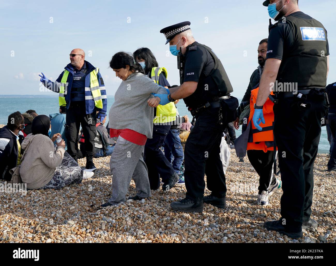 A heavily pregnant lady is helped by police officers as a group of people thought to be migrants walk up the beach in Dungeness, Kent, after being rescued in the Channel by the RNLI following following a small boat incident. Picture date: Thursday September 22, 2022. Stock Photo