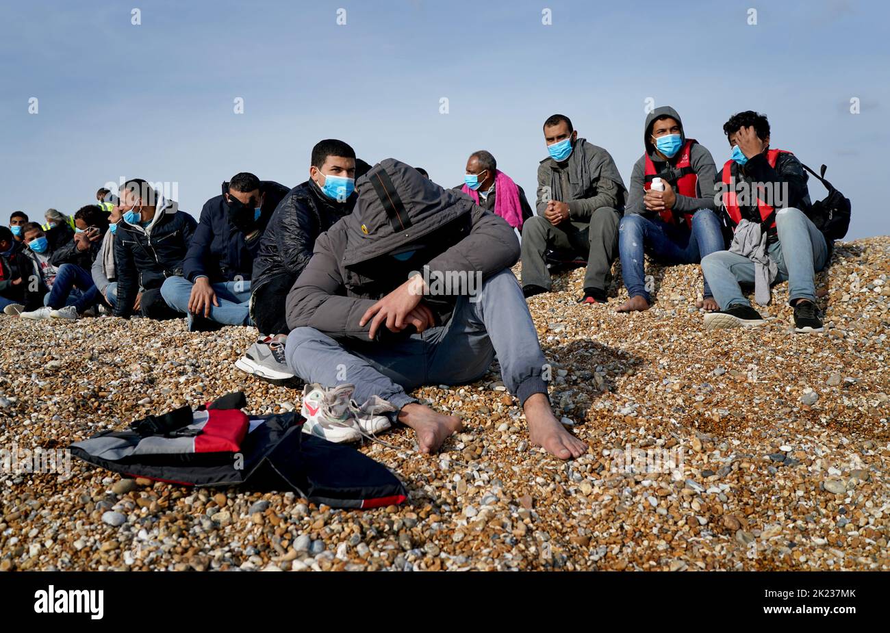 A group of people thought to be migrants rest on the beach after arriving in Dungeness, Kent, following being rescued in the Channel by the RNLI during a small boat incident. Picture date: Thursday September 22, 2022. Stock Photo