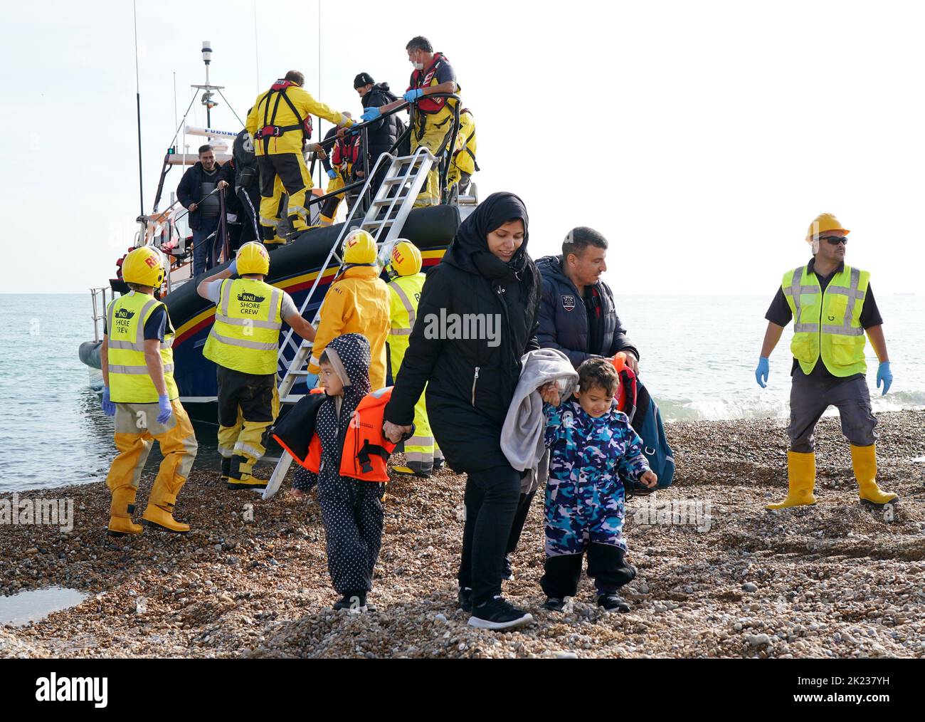 EDITORS NOTE: The PA Picture Desk has been unable to gain the necessary permission to photograph children under 16 on issues involving their welfare. This image has been provided unpixelated for customers to pixelate in their own style A young family are helped to shore as a group of people thought to be migrants arrive in Dungeness, Kent, after being rescued in the Channel by the RNLI following following a small boat incident. Picture date: Thursday September 22, 2022. Stock Photo