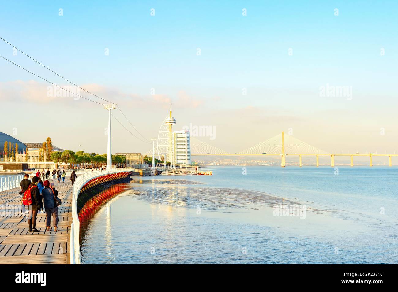 LISBON, PORTUGAL - NOVEMBER 11, 2021: Vasco da Gama bridge and hotel of modern futuristic architecture, people at promenade in sunset light, Lisbon, P Stock Photo