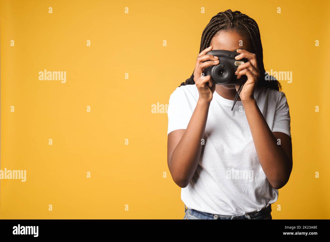 African-american woman taking photo of you. Female holding polaroid camera and pushing button standing isolated on yellow, making instant photo with retro camera Stock Photo