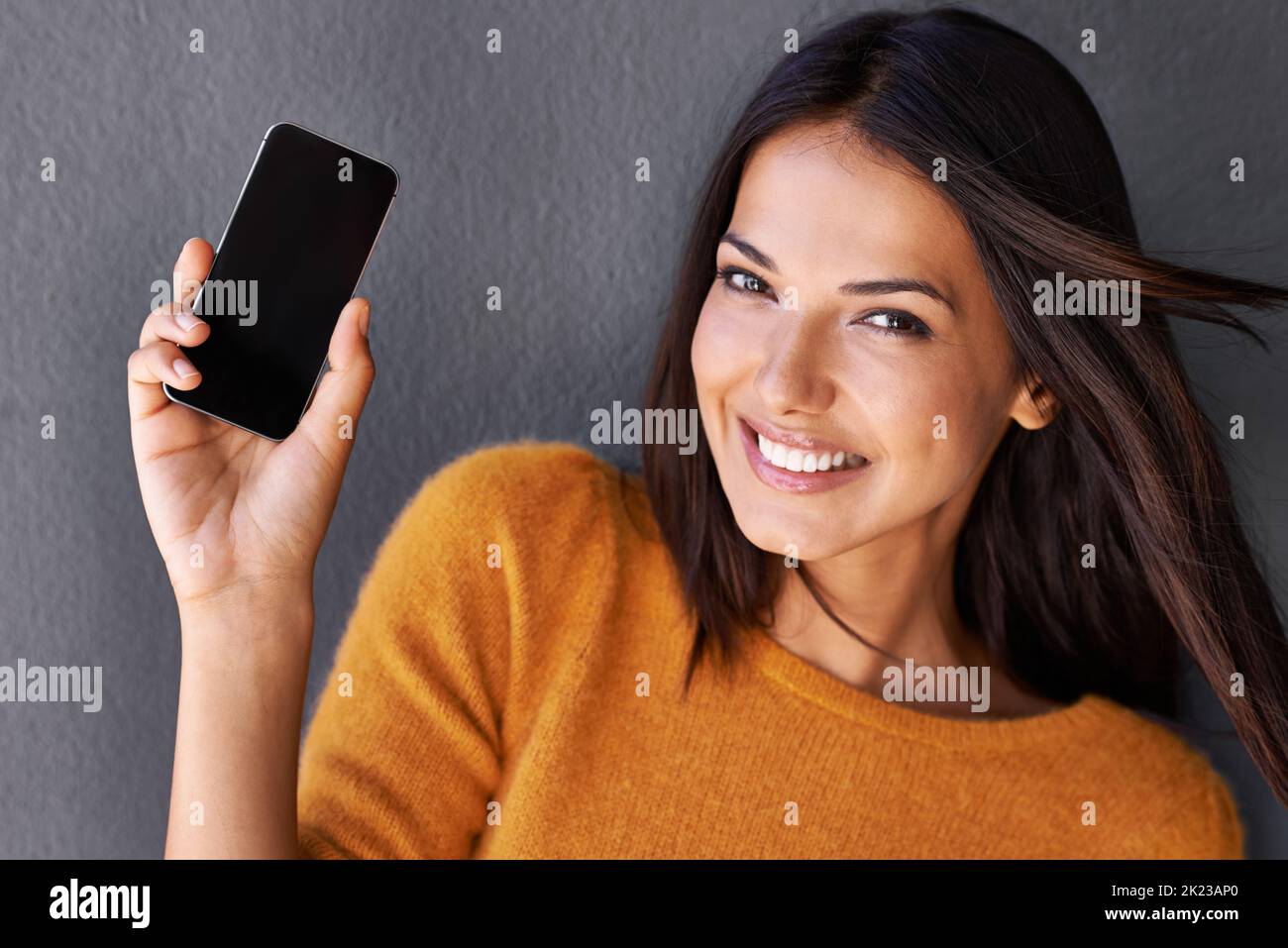 This makes staying connected easier. Closeup portrait of an attractive young woman holding up a mobile phone. Stock Photo