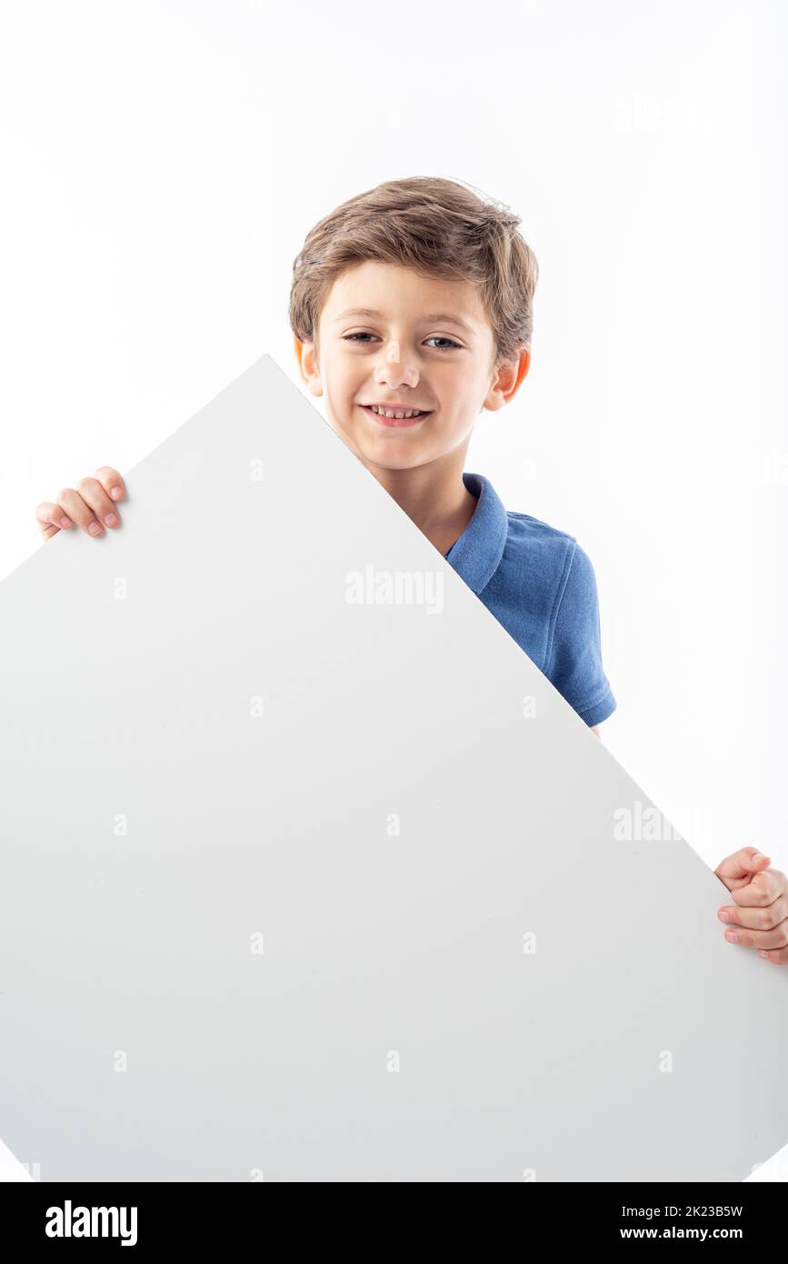Smiling Caucasian boy showing a white advertising poster with space for text, on a white background. Stock Photo