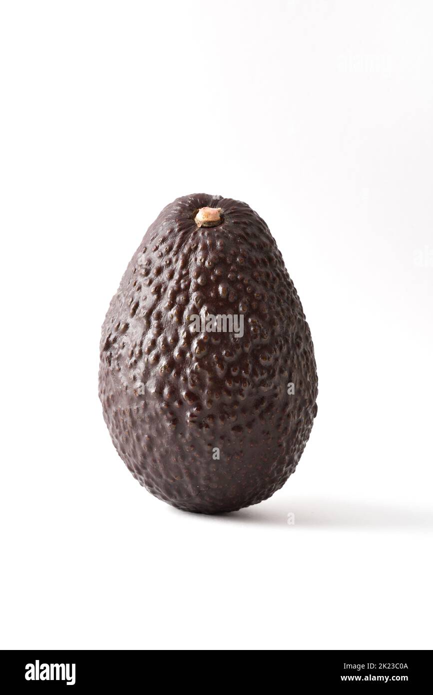 Detail of whole ripe avocado textured on white table and white isolated background.  Vertical composition. Stock Photo