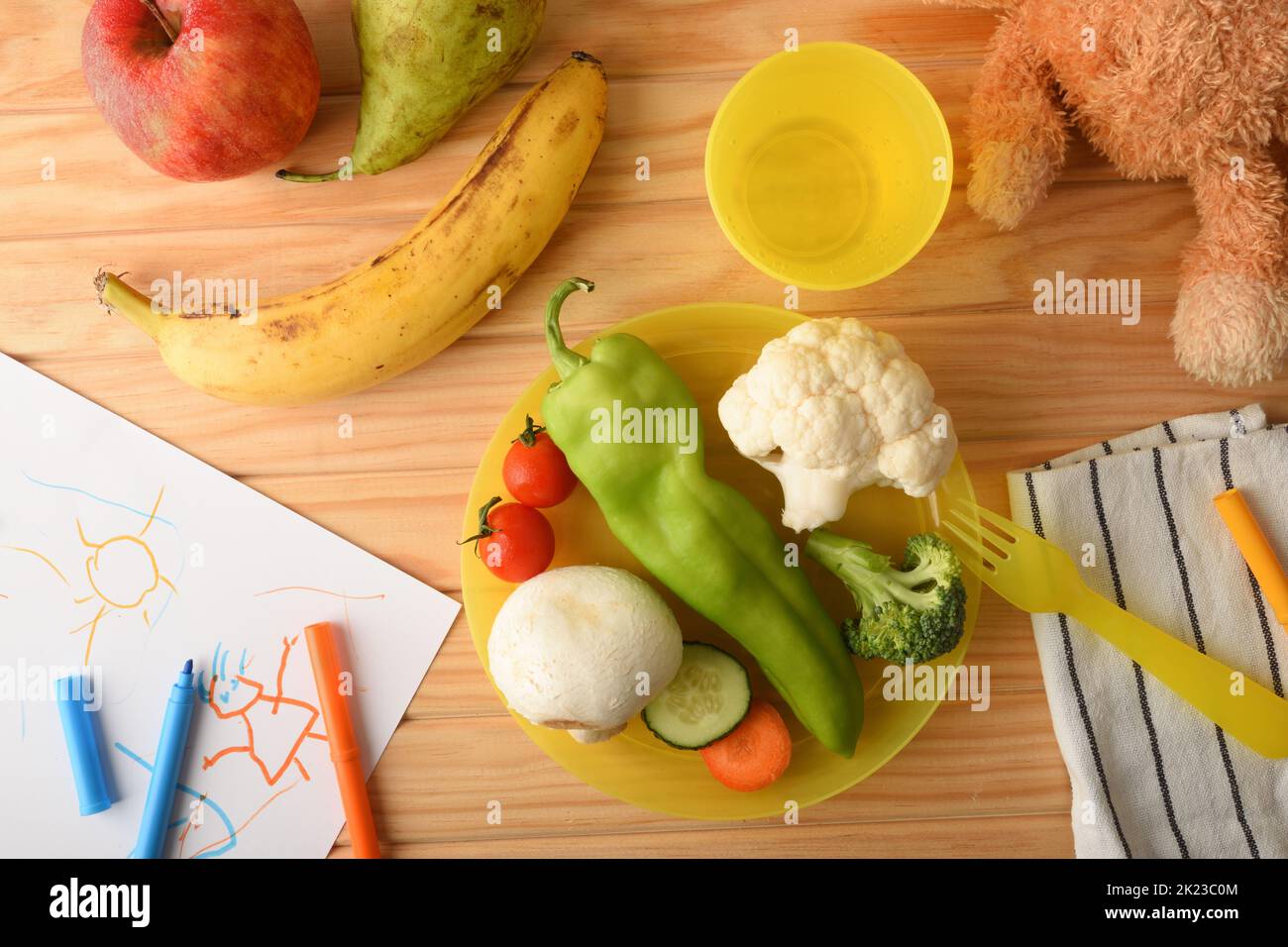 Concept of fun fruit and vegetables served in plastic containers on a wooden table prepared for a child with children's objects. Top view. Stock Photo