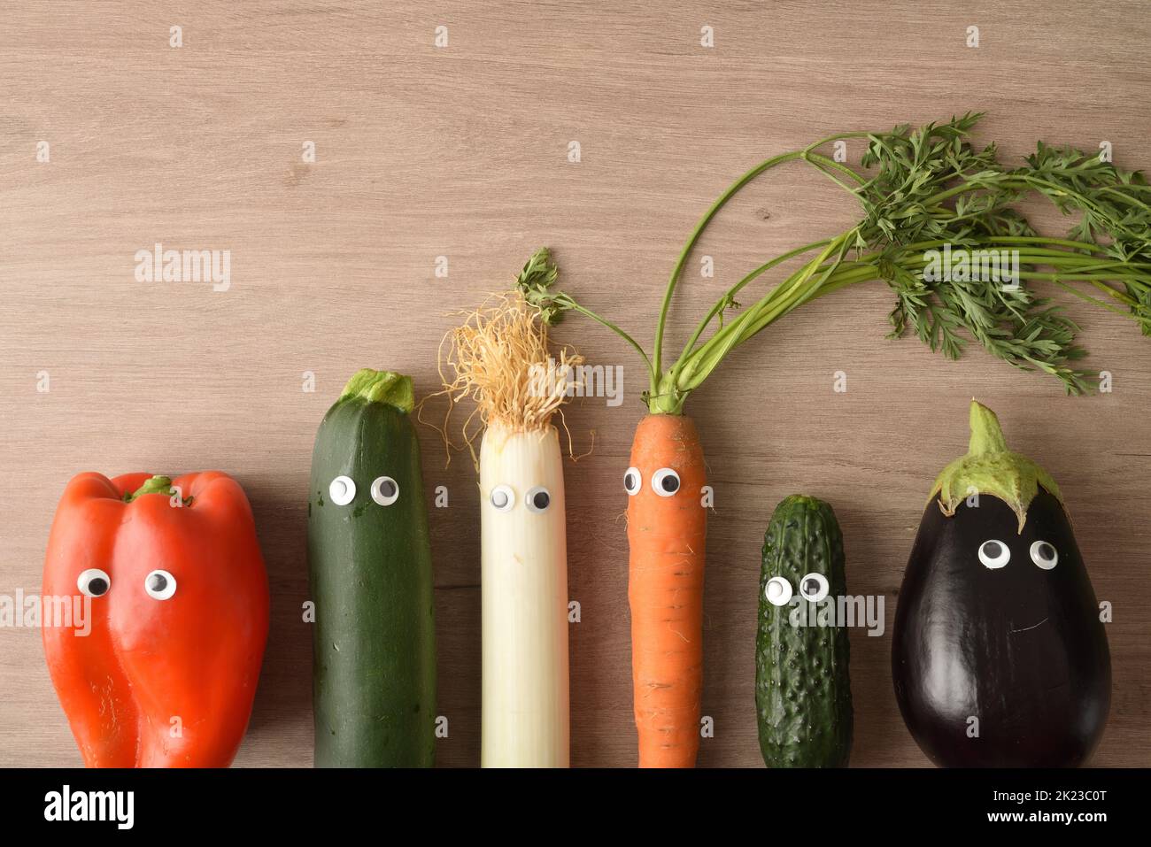 Background with funny vegetables with eyes on wooden table. Healthy infant nutrition. Top view. Stock Photo