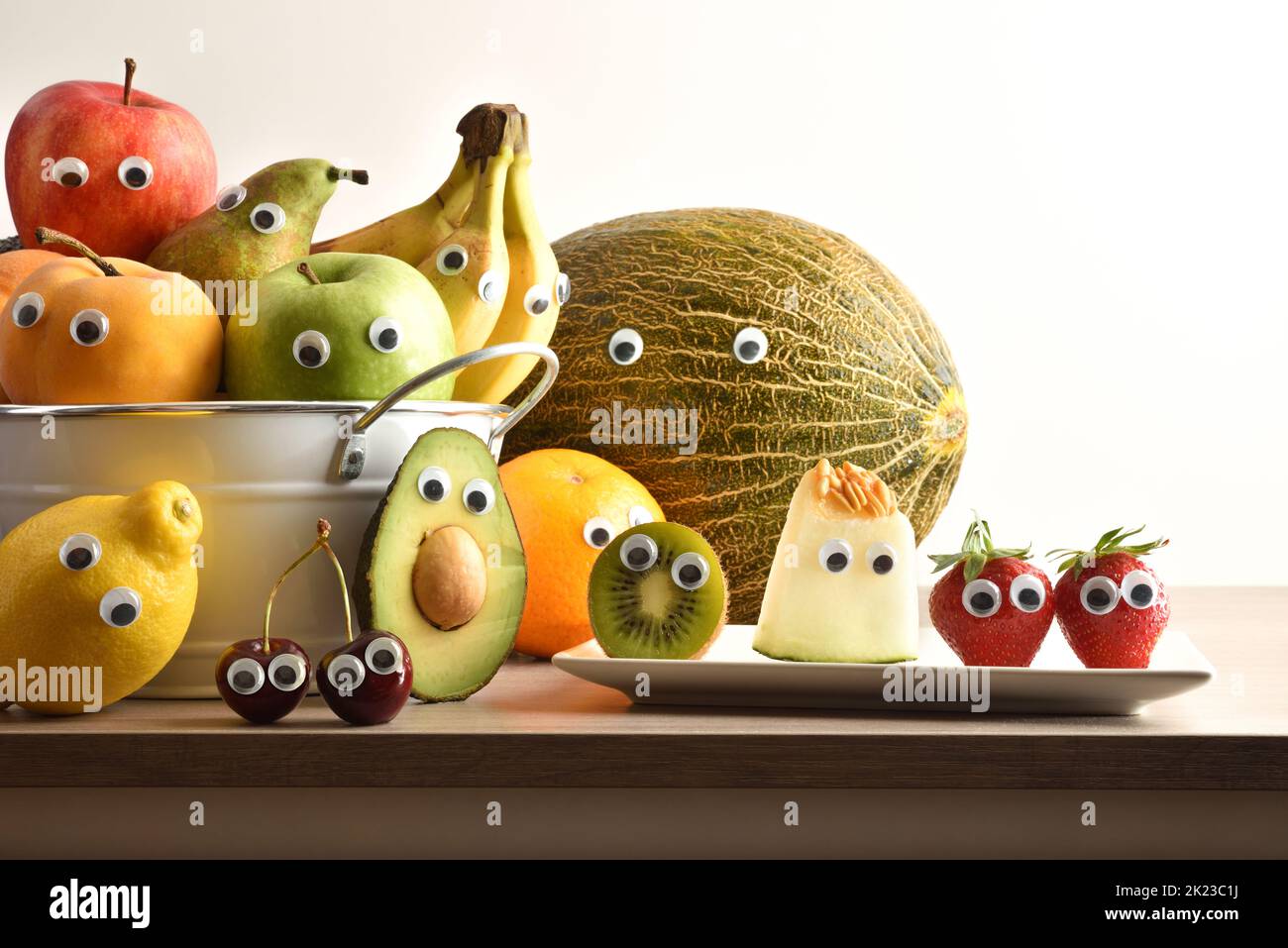 Group of fruits with eyes in containers on wooden bench and white isolated background. Fruits and vegetables child healthy eating concept. Stock Photo