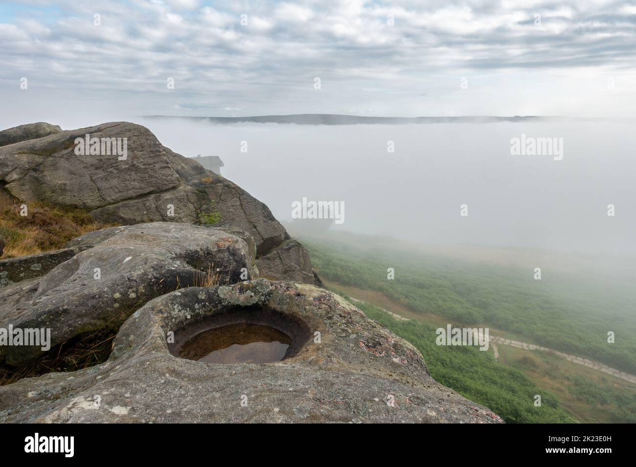 A cloud inversion in Wharfedale leads to a mist filled valley and an atmospheric view of the Cow and Calf Rocks on Ilkley Moor, West Yorkshire, Englan Stock Photo