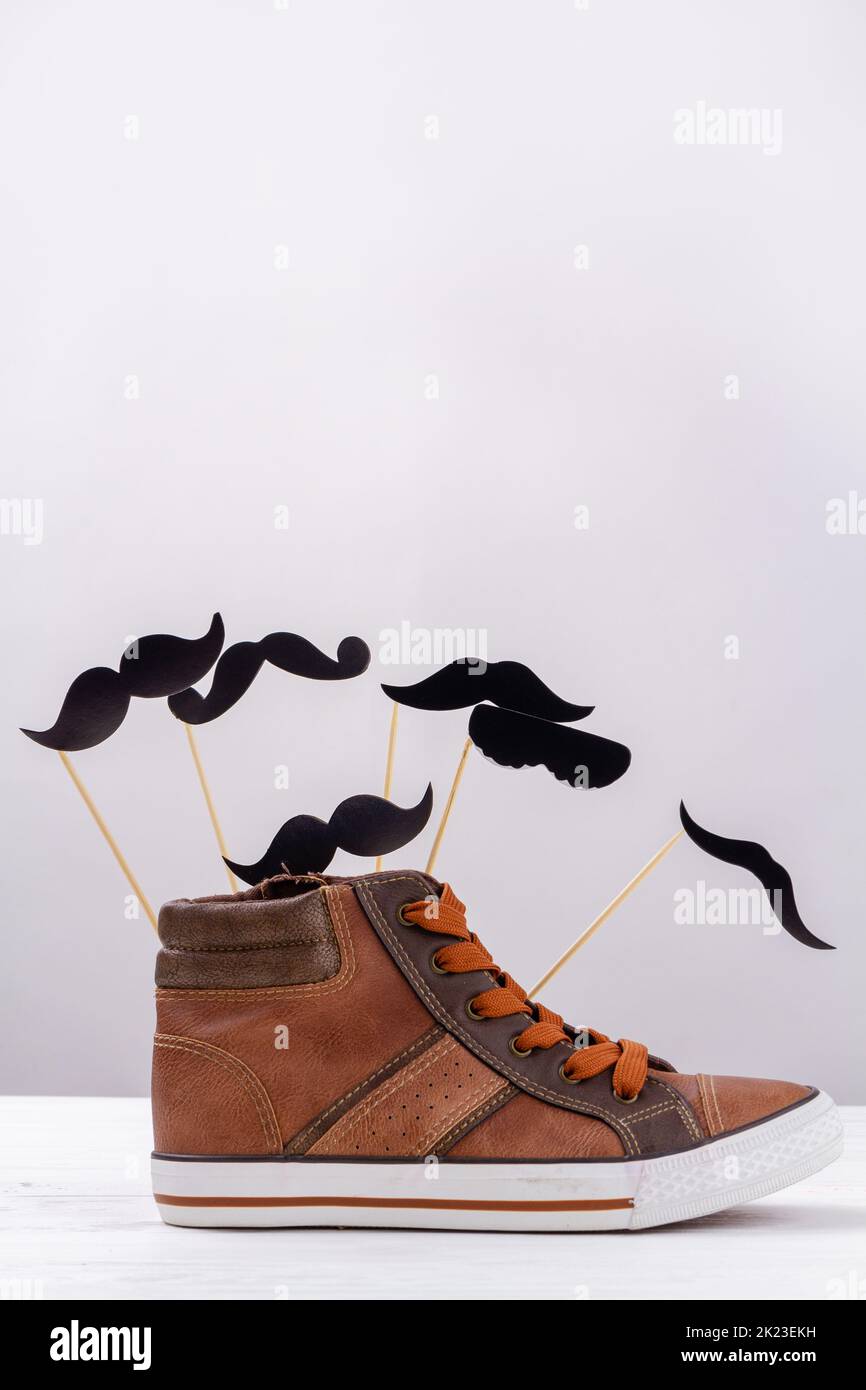 Vertical shot of brown sneaker with cartoon moustaches. Mens shoe with copy space on white. Stock Photo