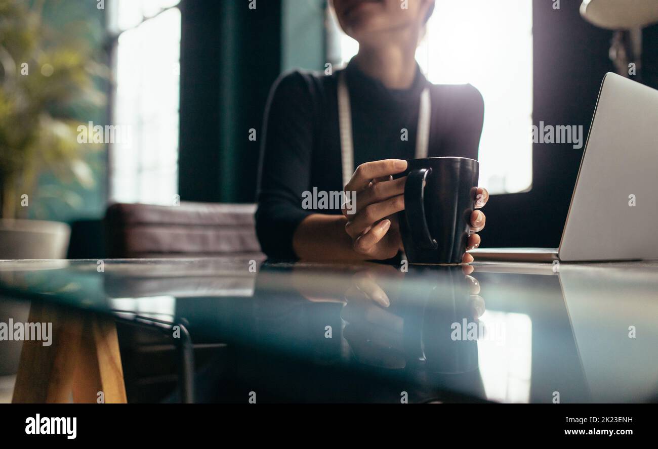 Female hand holding cup of coffee. Coffee mug on table with woman. Stock Photo