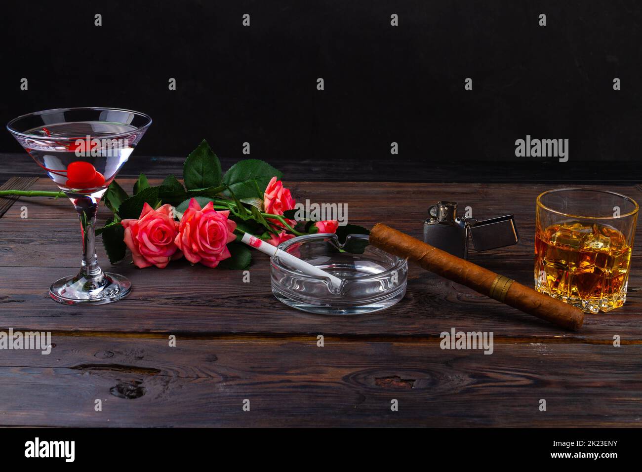 Alcoholic cocktails for man and woman on wooden desk. Glass of whiskey with a cigar on wooden table. Bouquet of flowers and cigarette in ashtray. Stock Photo