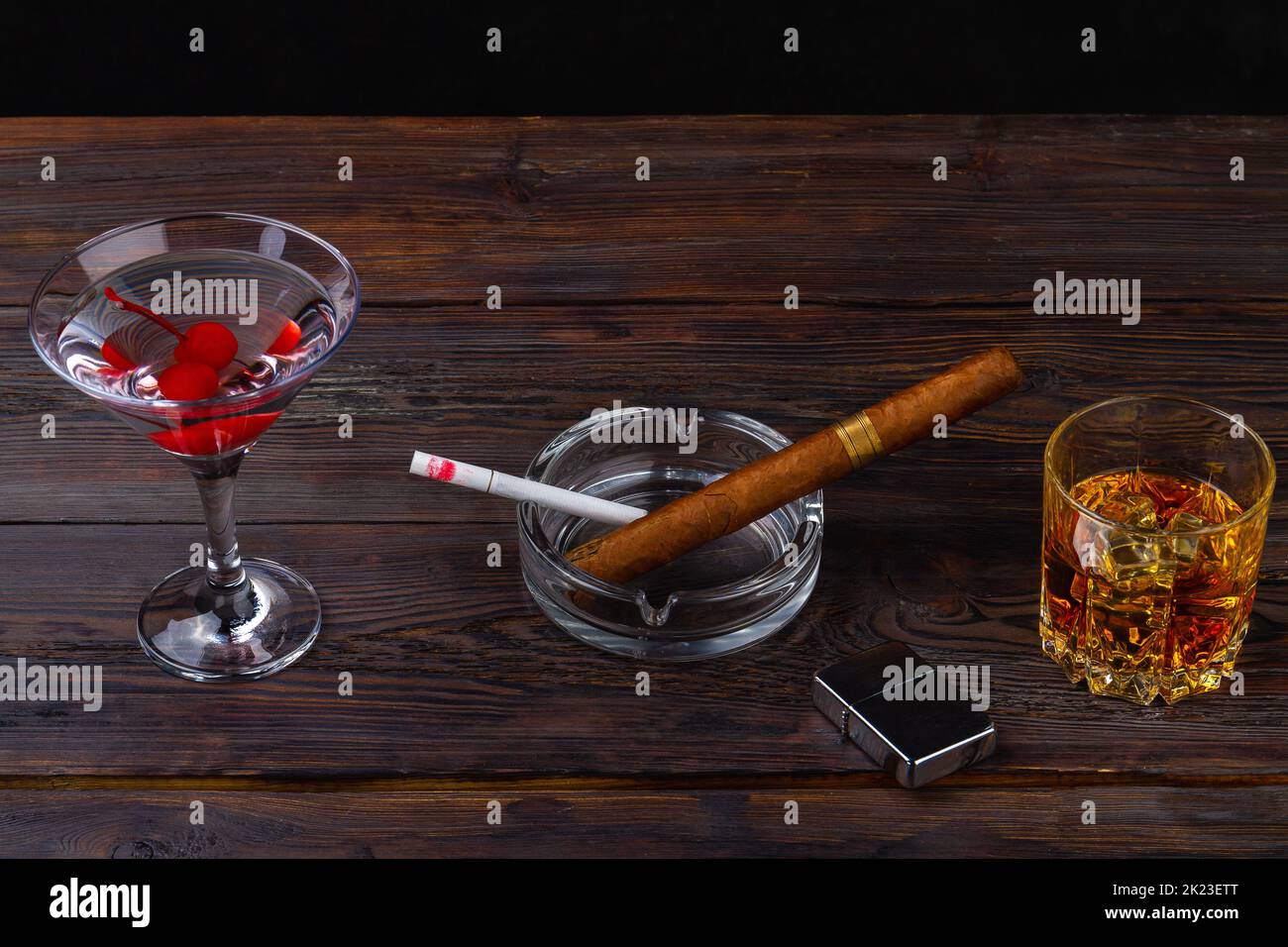 Alcoholic cocktails and cigarettes on brown desk. Cigar and cigarette in ashtray. Glass of whiskey and martini. Stock Photo