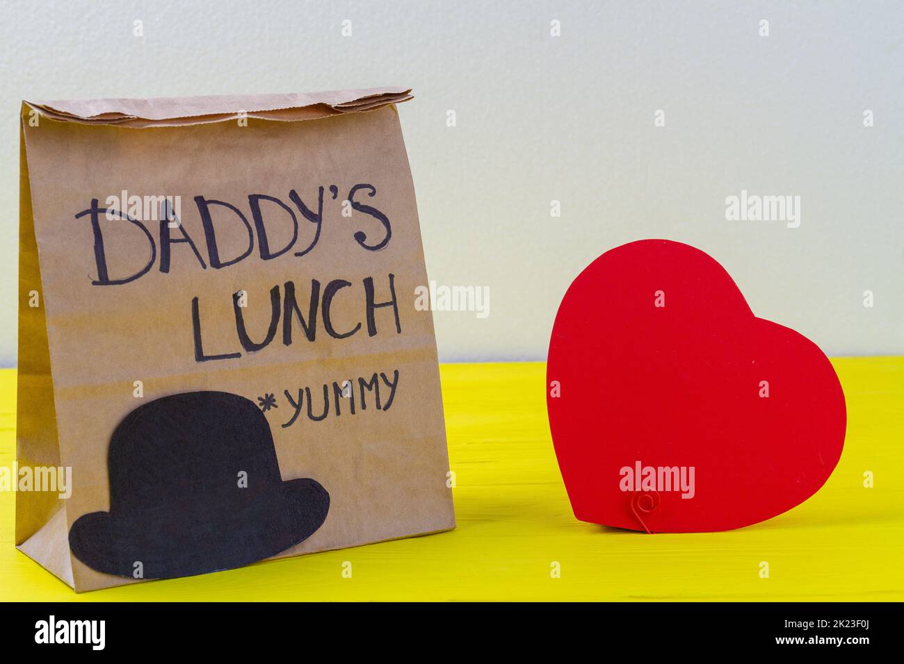 Paper bag and red heart on yellow wooden desk. Care and love for father concept. Stock Photo