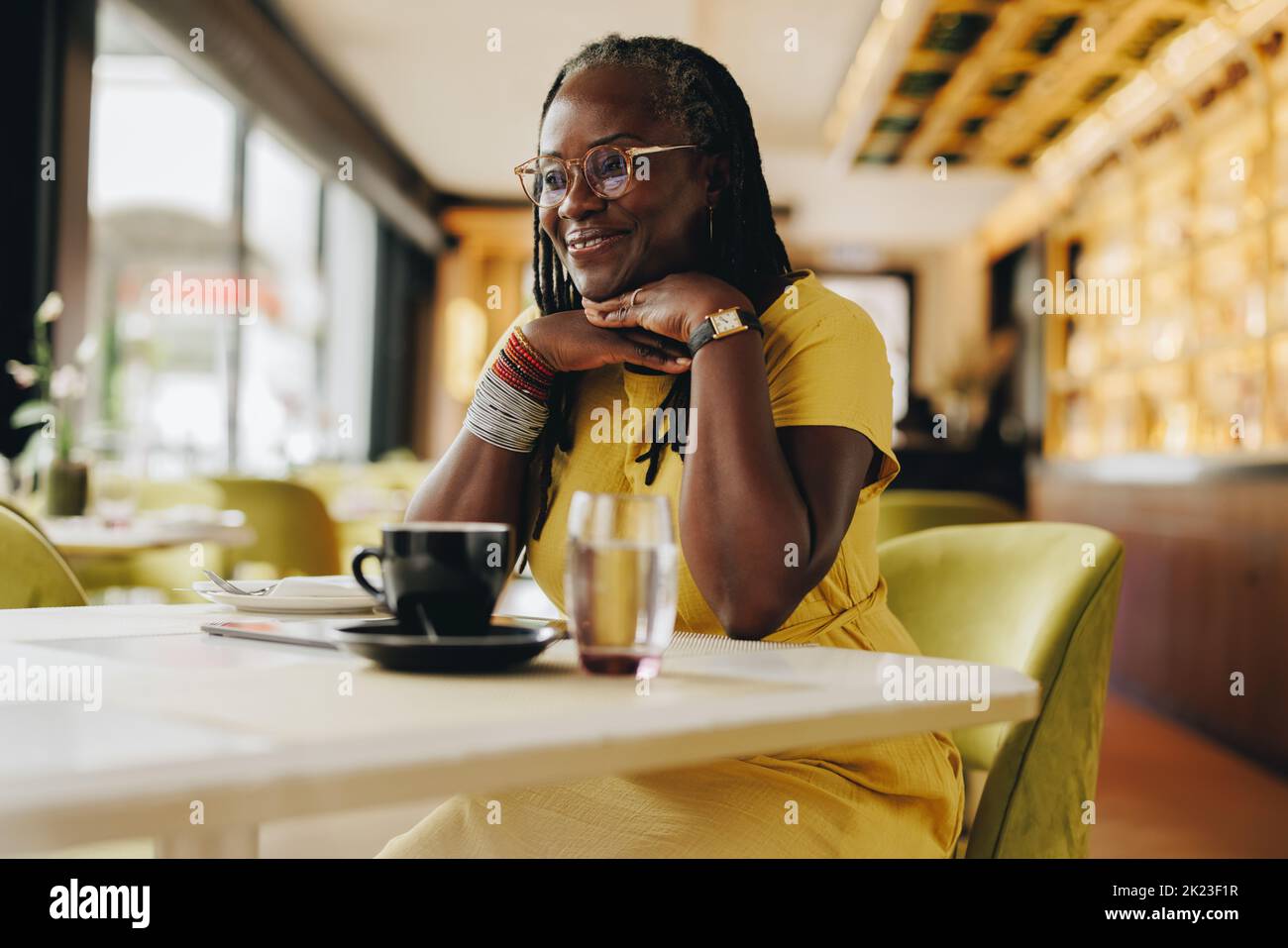 Happy mature woman looking away with a smile while sitting in a cafe. Cheerful woman with dreadlocks spending some time alone in a restaurant. Stock Photo