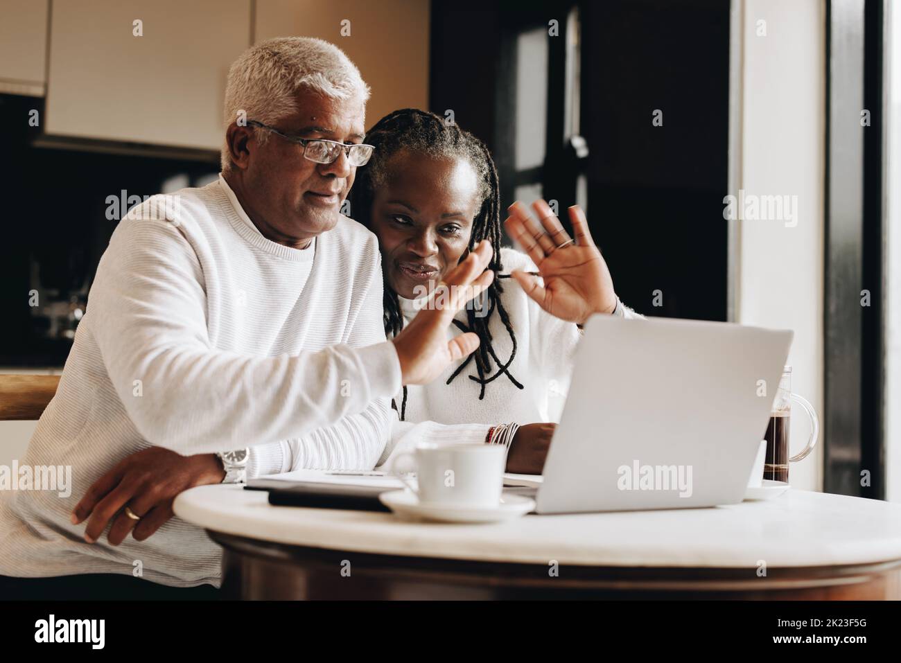 Senior couple waving their hands during a video call in their home. Mature couple having a virtual meeting with a retirement consultant. Ethnic senior Stock Photo