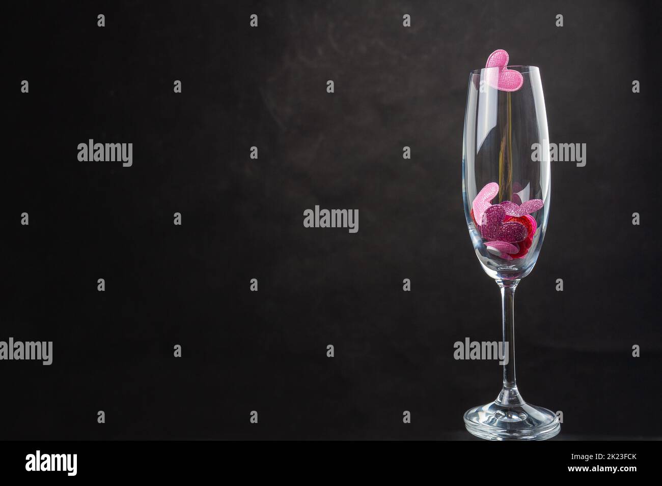 Champagne glass filled with sequin hearts. Copy space on black background. Stock Photo