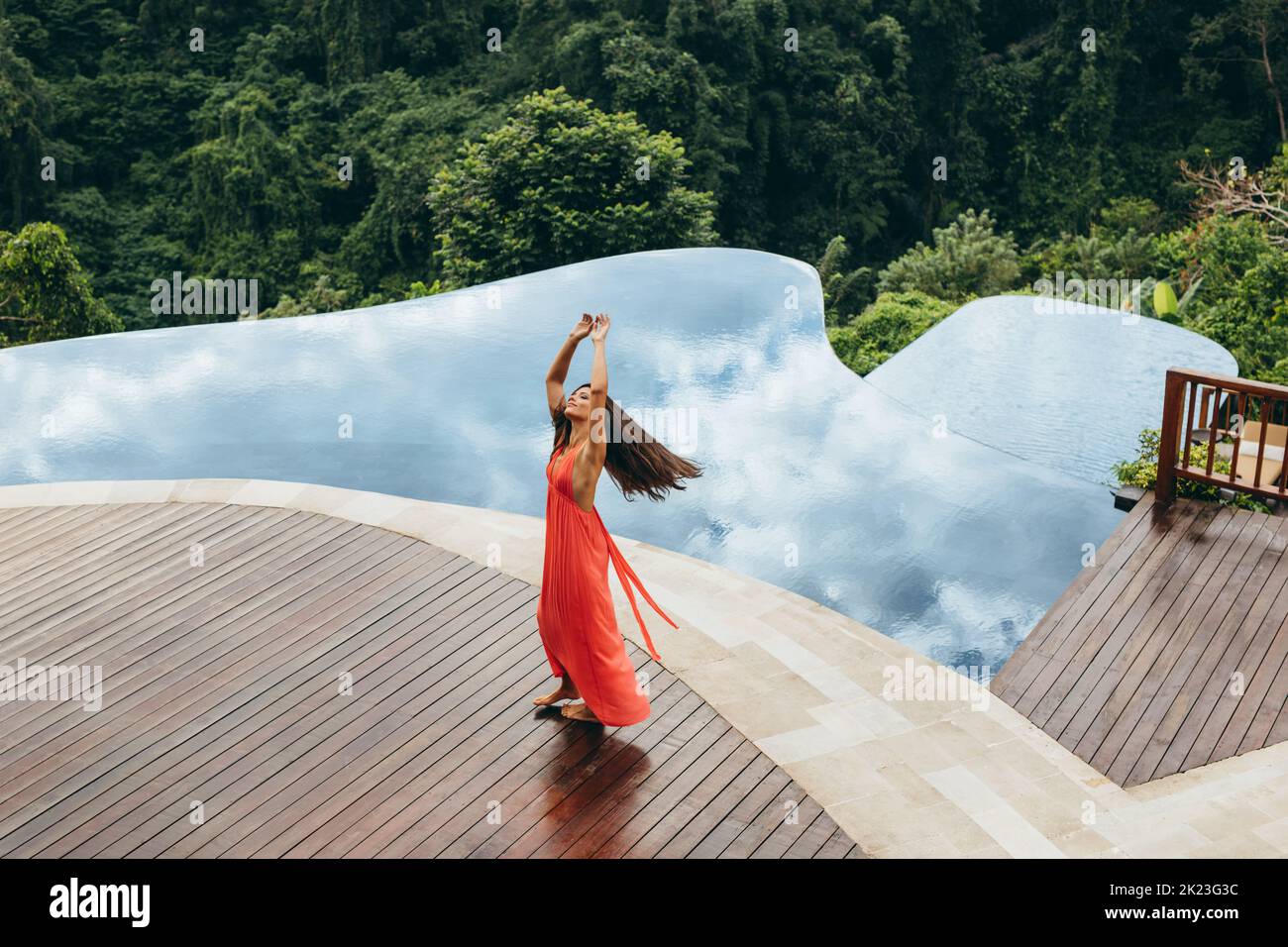 Shot of beautiful young woman dancing near swimming pool. Female enjoying at poolside of holiday resort. Stock Photo