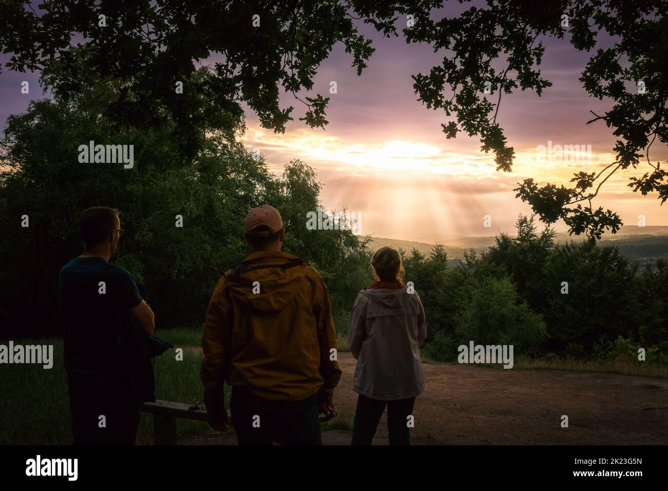 Three people watching the sun going down creating crepuscular rays in Wharfedale, Otley Chevin, West Yorkshire, England, UK Stock Photo