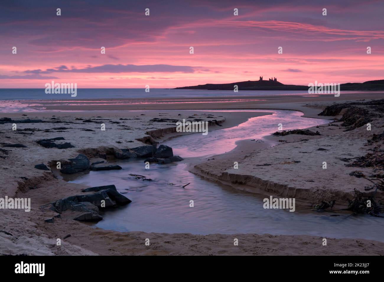 Pink sunrise over the beach at Embleton Bay on the Northumberland Coast of England, with Dunstanburgh Castle as a back drop Stock Photo