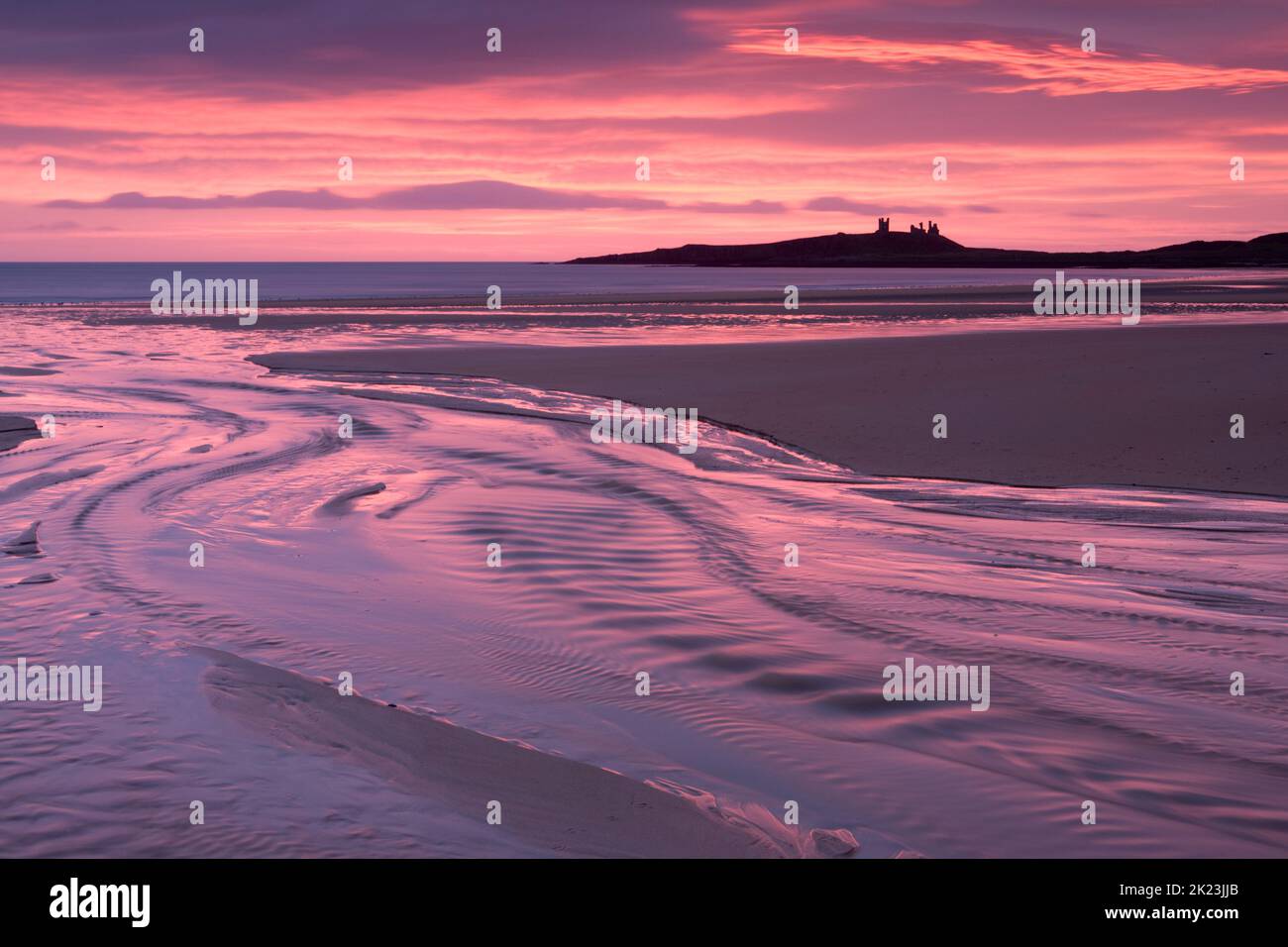 Pink sunrise over the beach at Embleton Bay on the Northumberland Coast of England, with Dunstanburgh Castle as a back drop Stock Photo