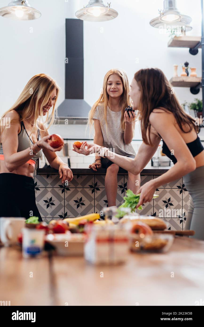 Sporty girls in good spirits in the kitchen eating fruits. Stock Photo