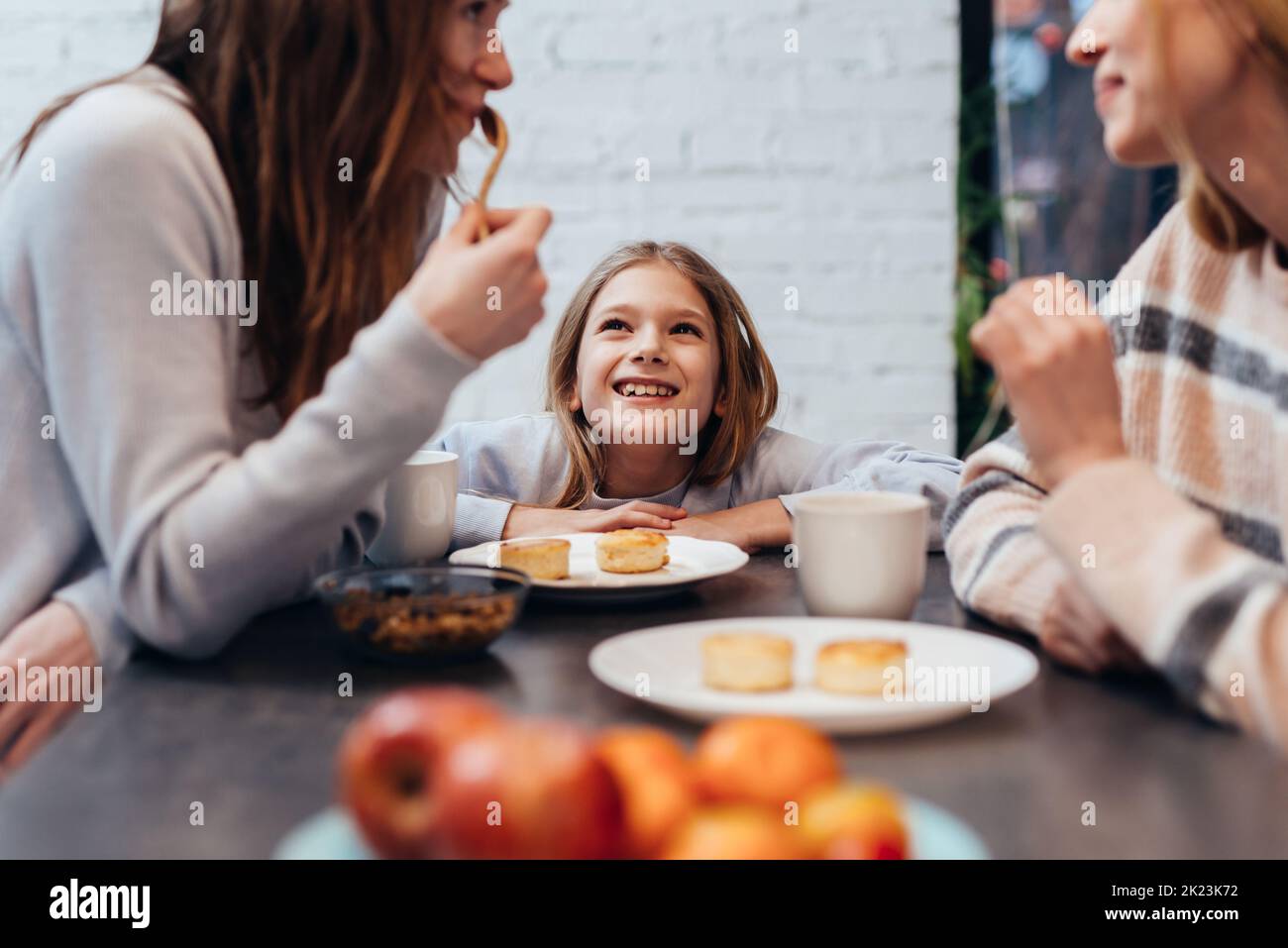 Girl sits between the young women at the kitchen table and listens to their conversations. Stock Photo