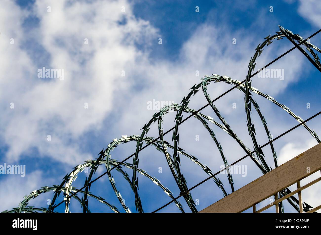 Chain link fence with barbed wire and razor wire against blue sky. Stock Photo
