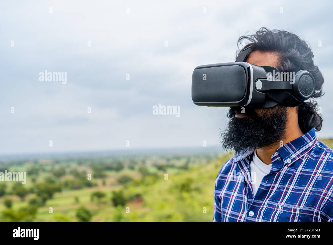 focus on VR, Young beard man using virtual reality headser on top of hill in rain with copy space - concept of technology, future and metaverse. Stock Photo