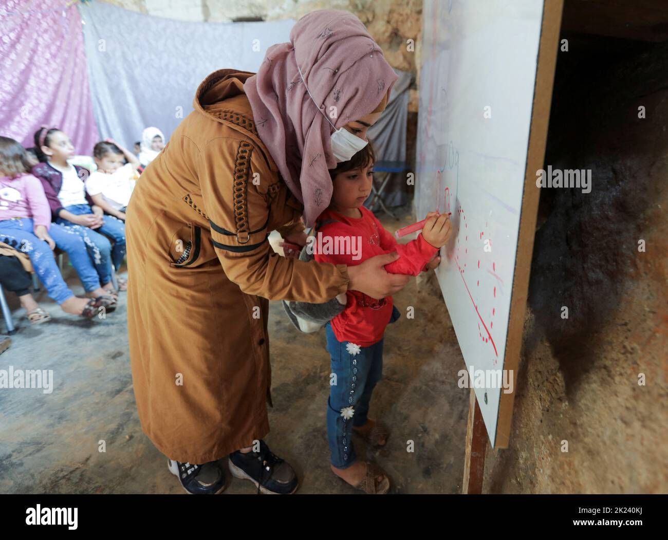 A teacher helps a student to write on a board inside a Byzantine castle that was transformed into a makeshift school for the internally displaced children in the opposition-held Idlib, Syria September 20, 2022. REUTERS/Khalil Ashawi Stock Photo