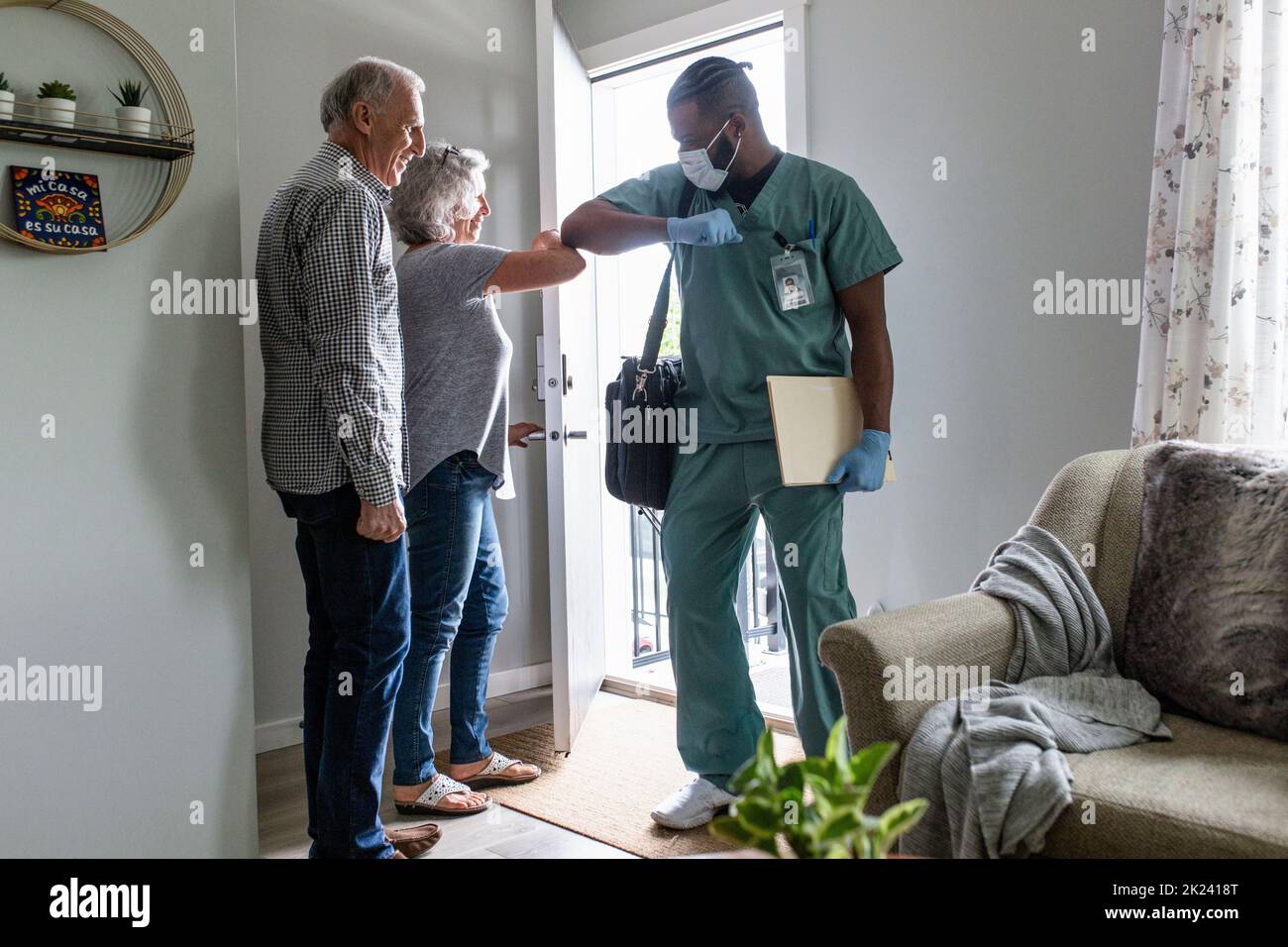 Home caregiver greeting senior couple with elbow bump at front door Stock Photo