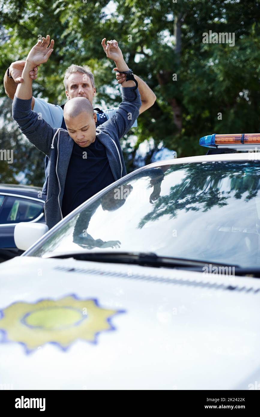 Put your hands in the air. a man standing with his hands in the air while a policeman is arresting him. Stock Photo