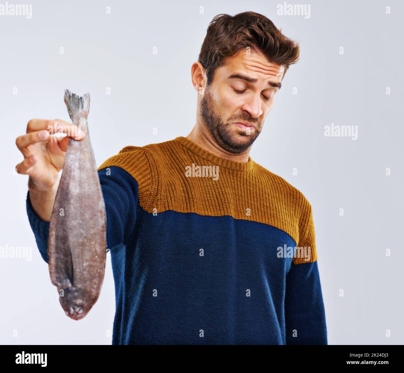 I hope it tastes better than it smells. Studio shot of a man showing disgust while holding a smelly fish. Stock Photo